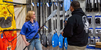 A customer is assisted by a store associate inside a West Marine store as he selects a kayak paddle