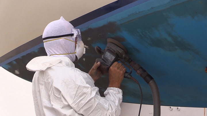 person using a electric sander with a vacuum system to remove the bottom paint on a boat