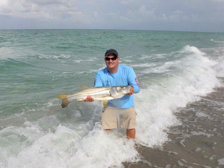 Author standing in surf holding fish and wearing sunglasses