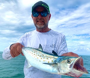 Man holding Spanish mackerel with mouth open showing teeth.