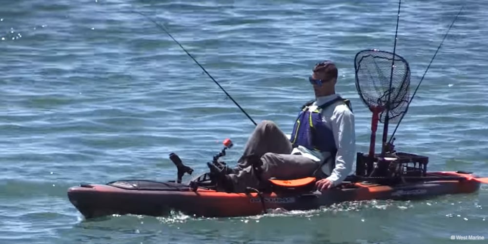 Angler on a pedal-drive sit-on-top fishing kayak rigged with rod holders, landing net, and fishing accessories