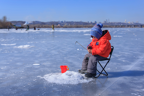 Little boy fishing through hole in ice