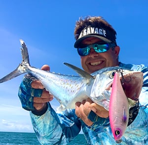 Man holding Spanish mackerel with lure hanging from mouth.