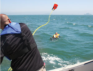 man using a throw rope bag to reach an overboard crew member