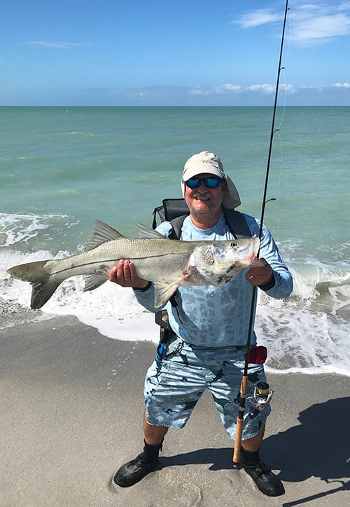 Author standing at edge of surf holding up fish
