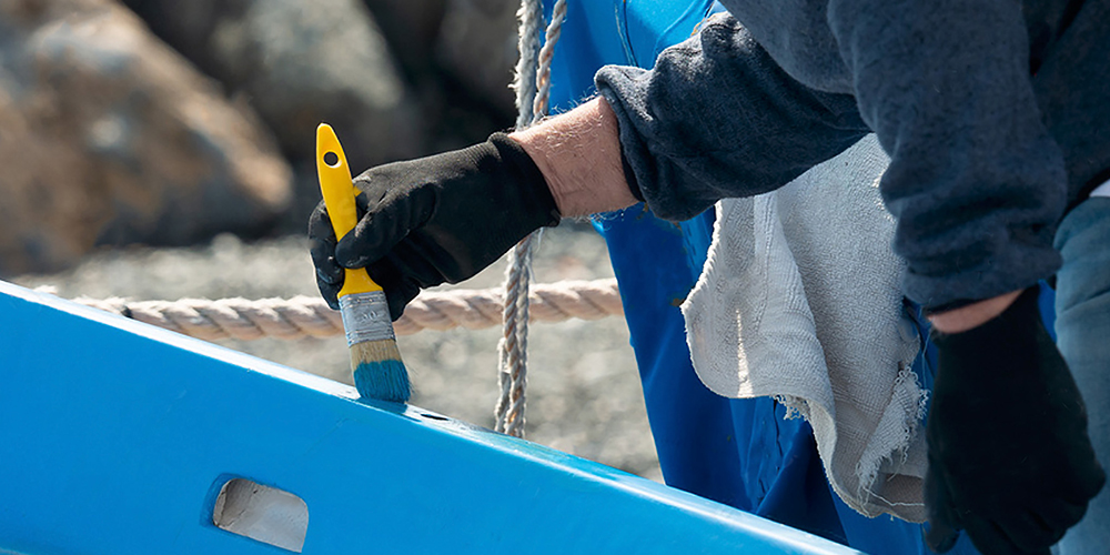 Arm brushing blue paint on to gunwale of boat