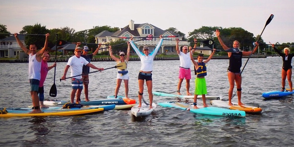 Group of paddleboarders on the water standing on their boards holding their paddles over their heads