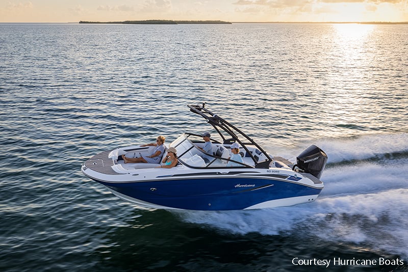 Deck boat speeding across water at sunset