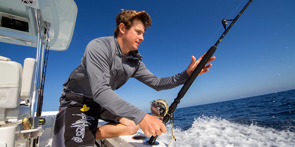 Young man grabbing trolling rod at stern of boat