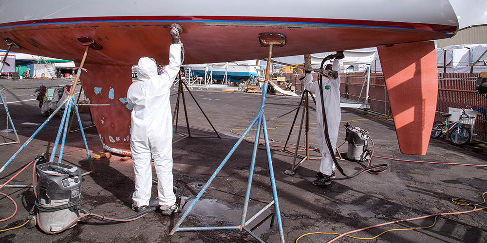 Workers sanding sailboat hull in boat yard.
