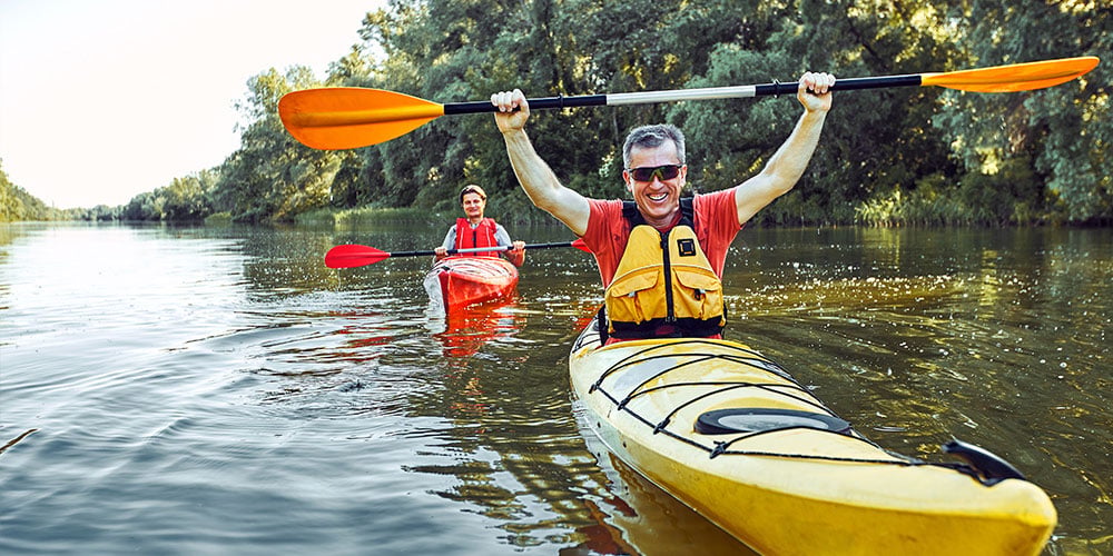 Man in a kayak facing camera holding paddle over his head