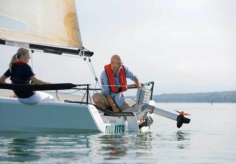 Man at stern of sailboat tilting electric outboard out of water