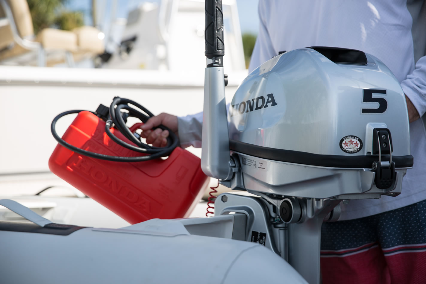 a 5 horsepower honda outboard attached to an inflatable boat with a person getting ready to attach the fuel tank
